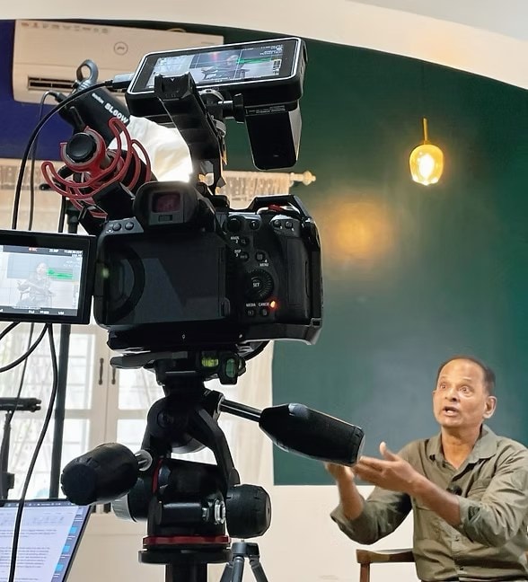Rigged camera with on-board monitor and shotgun mic, filming an interview subject on a green backdrop