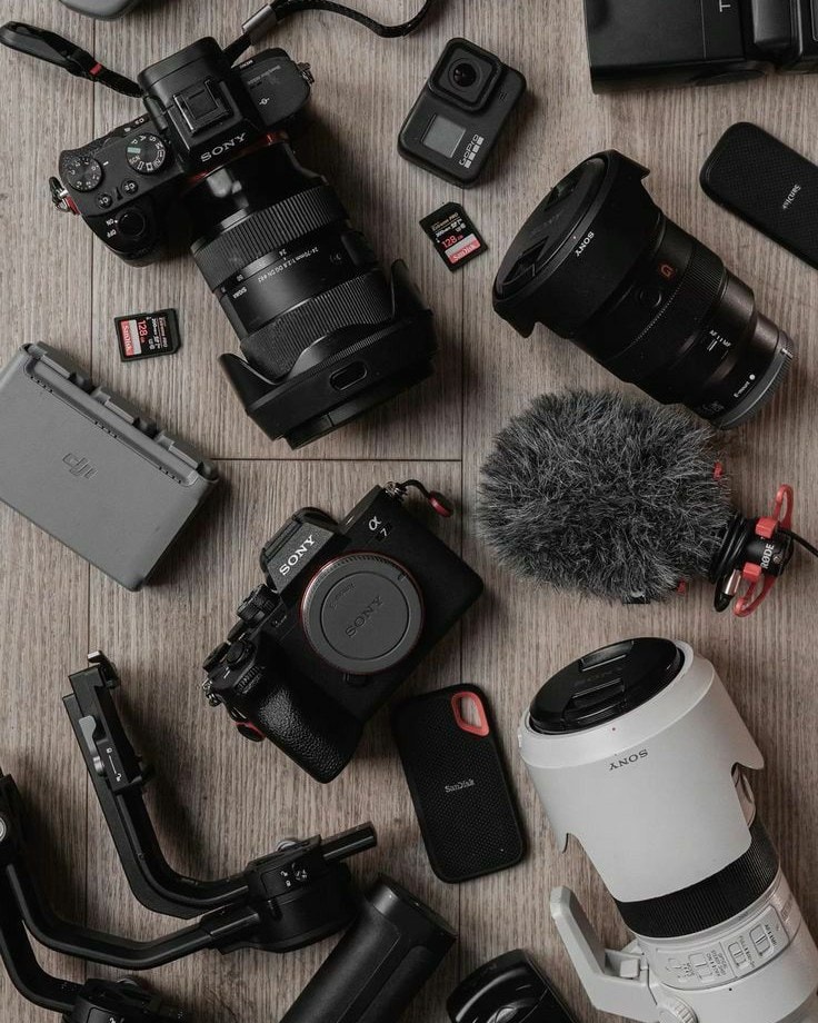 Camera bodies, lenses, a shotgun microphone, SSD and gimbal laid out on a wooden floor