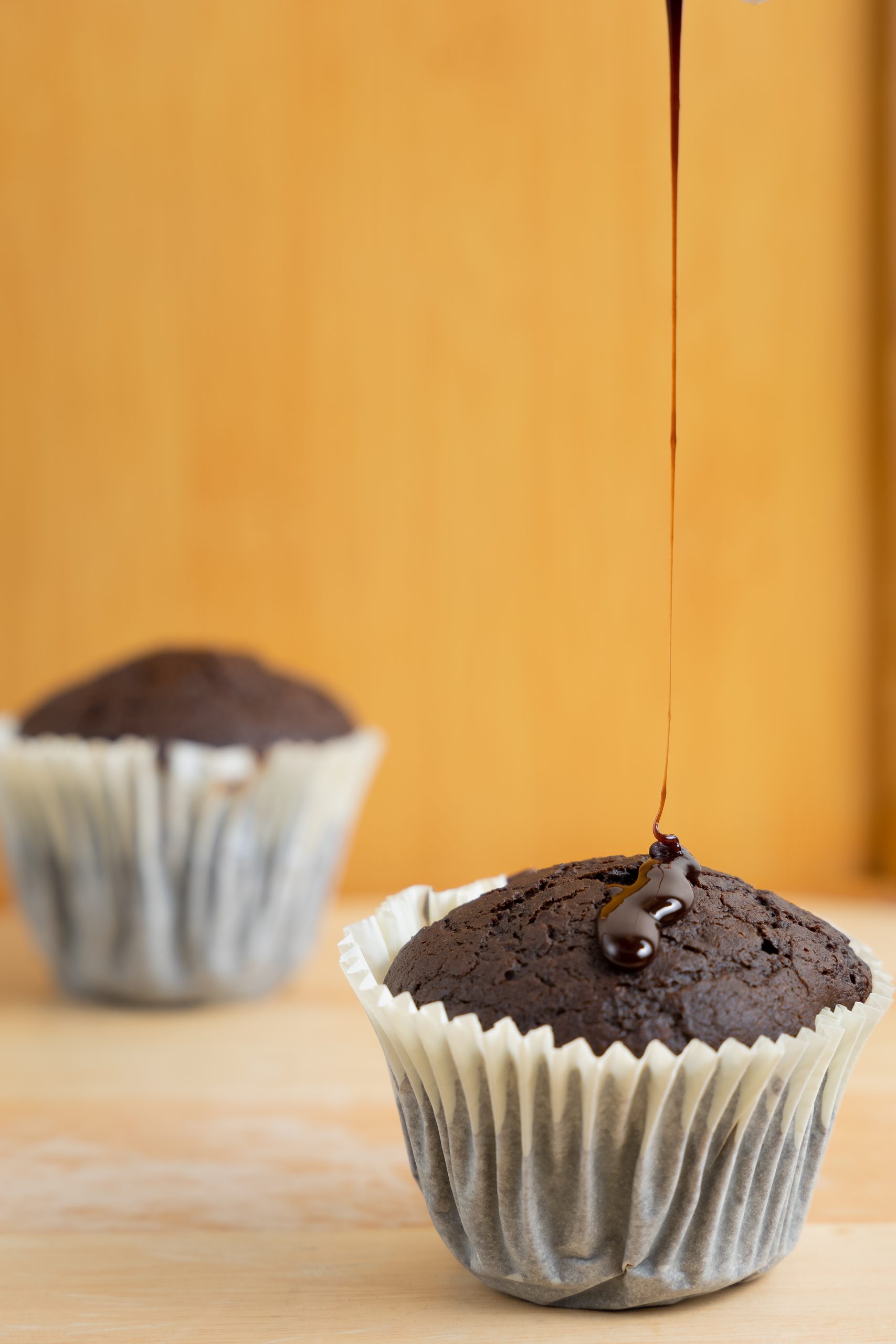 Chocolate muffin with sauce poured over it on an ochre ground