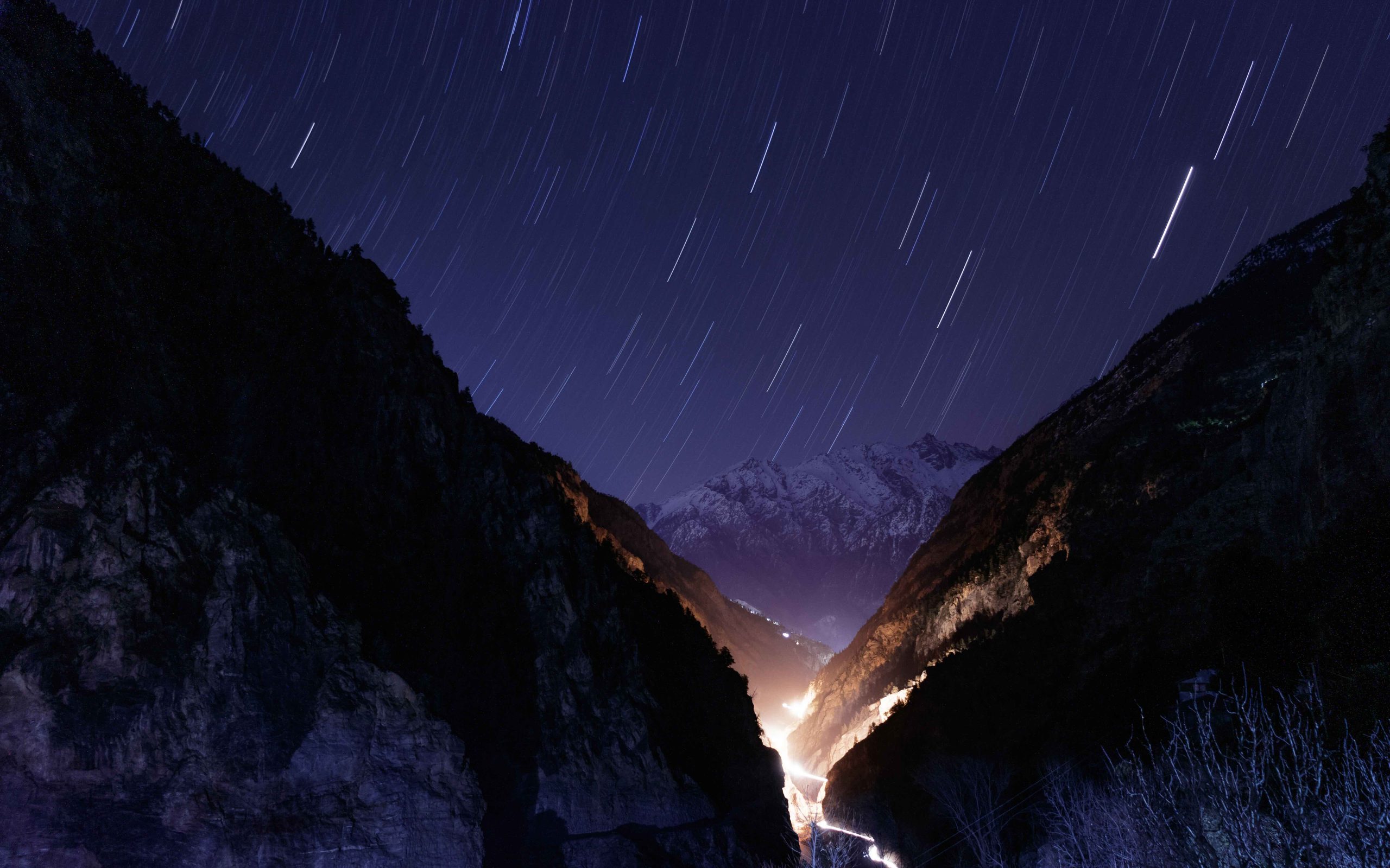 Star trails over a gorge with a lit road below