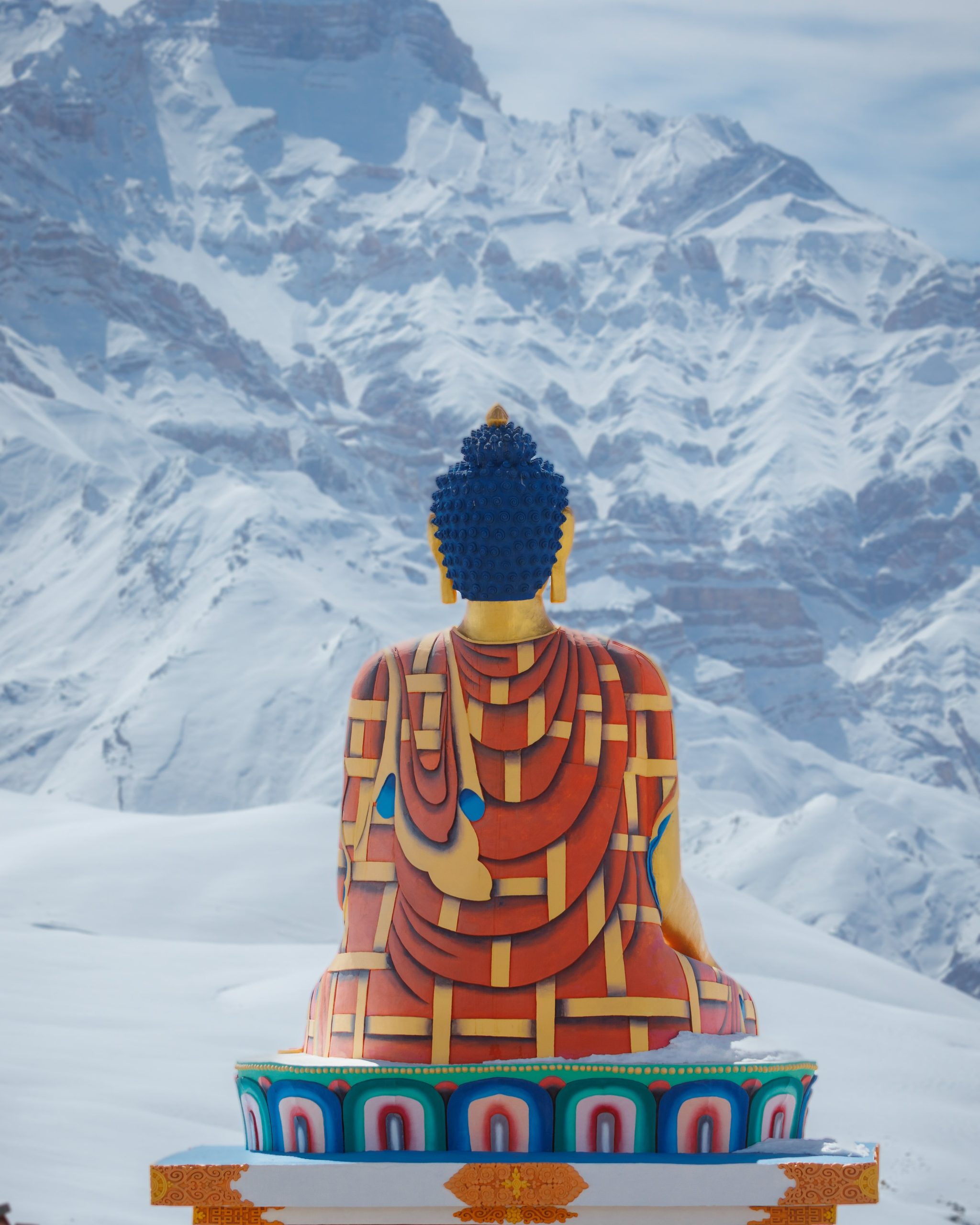 Painted Buddha statue before snow mountains