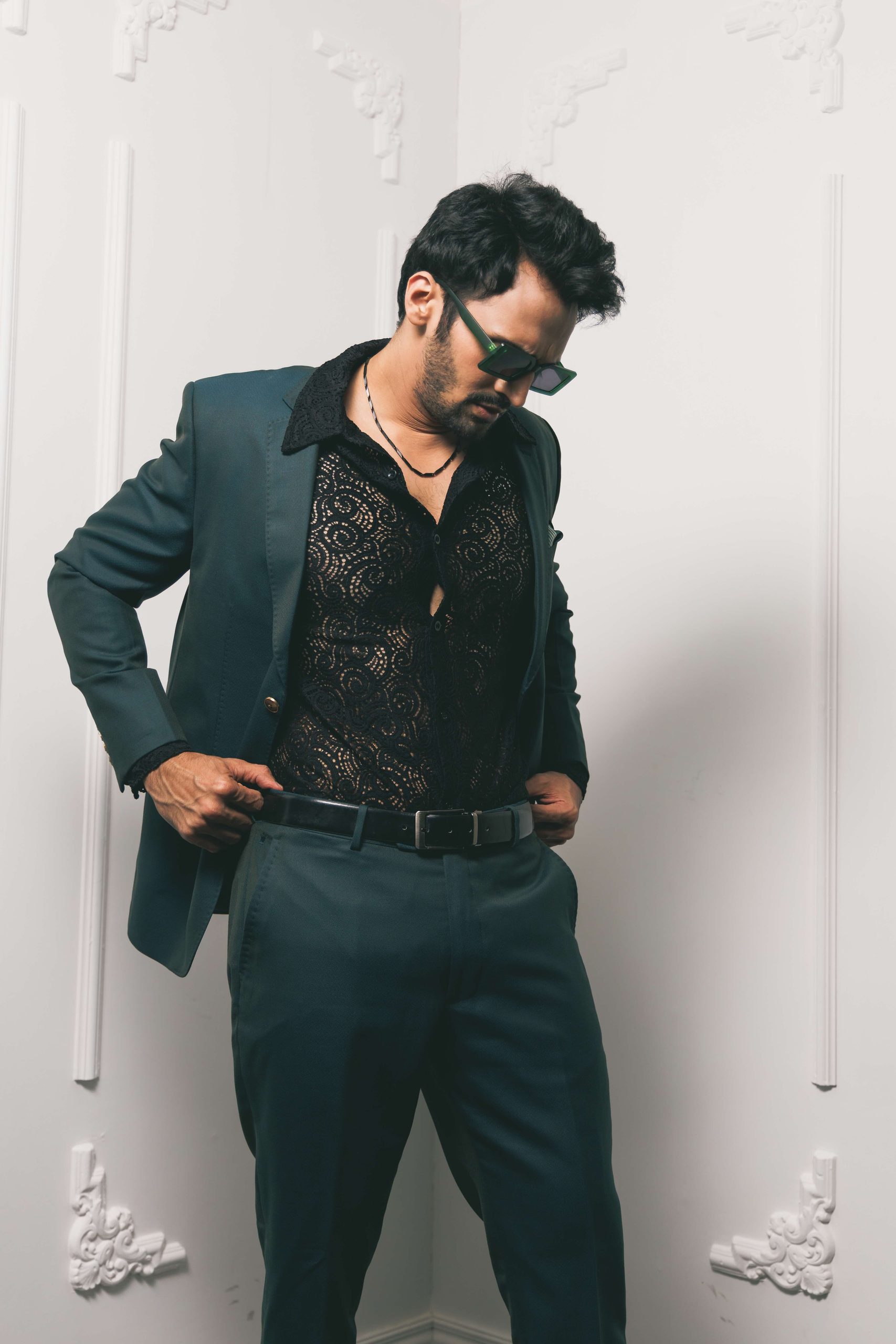 Model in a dark suit and sunglasses against a white panelled wall
